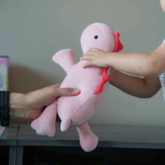 Child's hand reaching out to take a pink plush toy from an adult's hand.