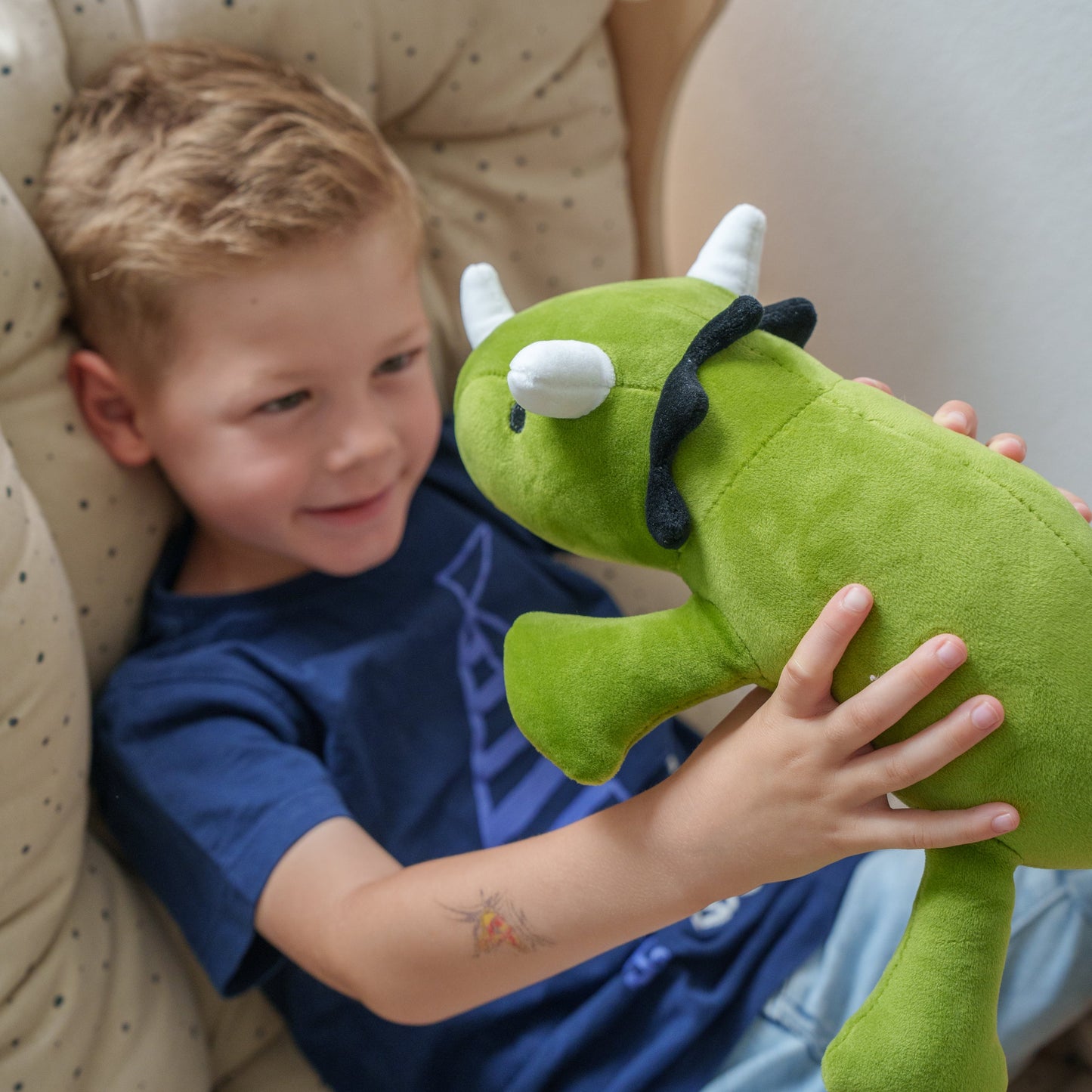 Child holding a green plush toy in a cozy indoor setting